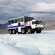 Mountains stand in the background of a heavy duty transport vehicle parked on the ice